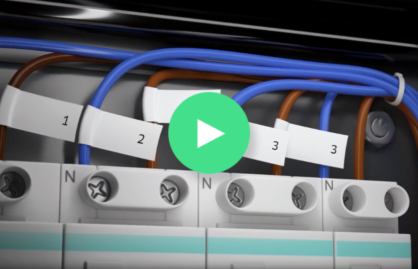 Close-up of labeled electrical wires connected to terminals, demonstrating the use of TZe label cartridges to clearly identify each wire. A green play button overlay appears in the center, highlighting how these durable labels help extend label life even in demanding environments.