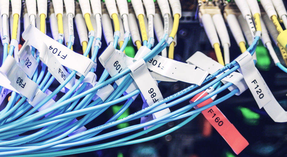 A group of wires plugged into a data center with a plethora of wire labels