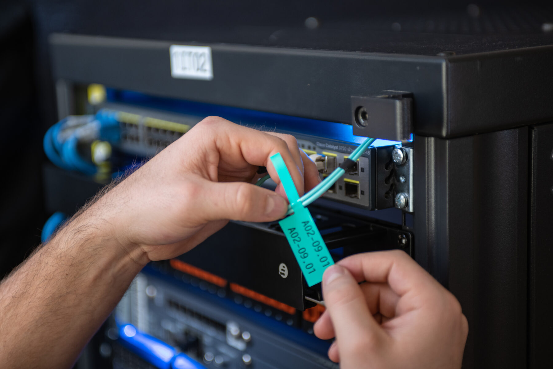 Male hands in front of an audio visual rack wrapping a cable flag around a wire