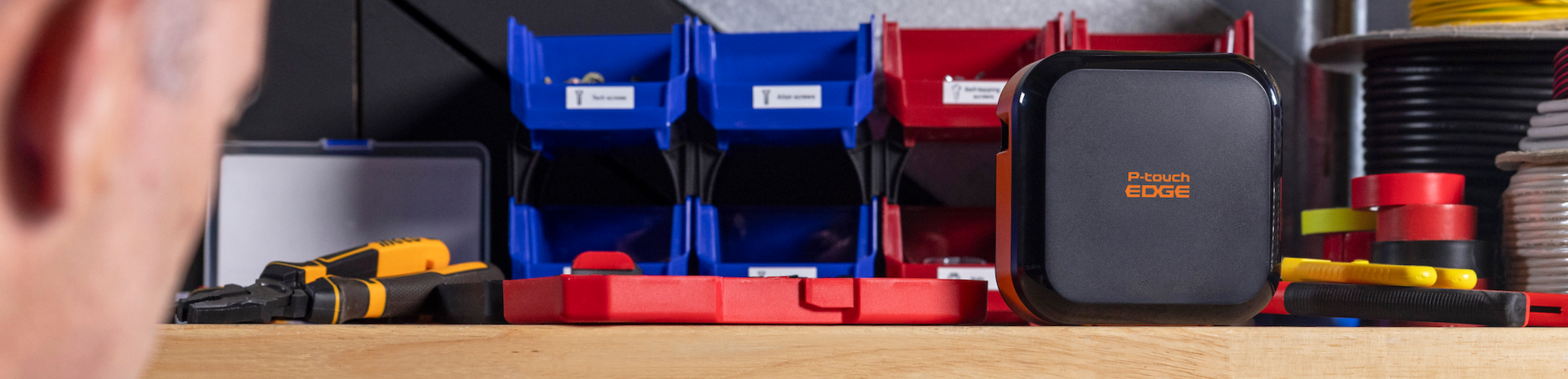 Close-up of a workbench with tools, storage bins, and the P-touch EDGE 720BT label maker at the center.
