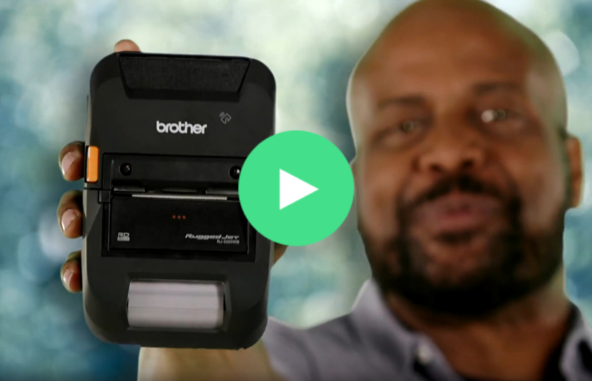 A person holds up a Brother RuggedJet 3200 mobile printer with a blurred green background.