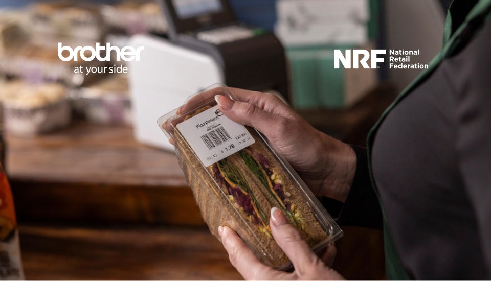 A person holds a packaged sandwich with a printed label in front of a Brother label printer at a store counter, showcasing retail innovation.
