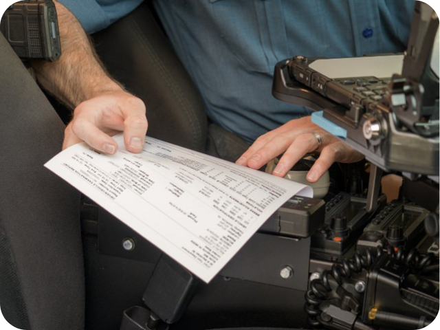 A person in uniform reviews a printed form inside a vehicle equipped with communication devices.