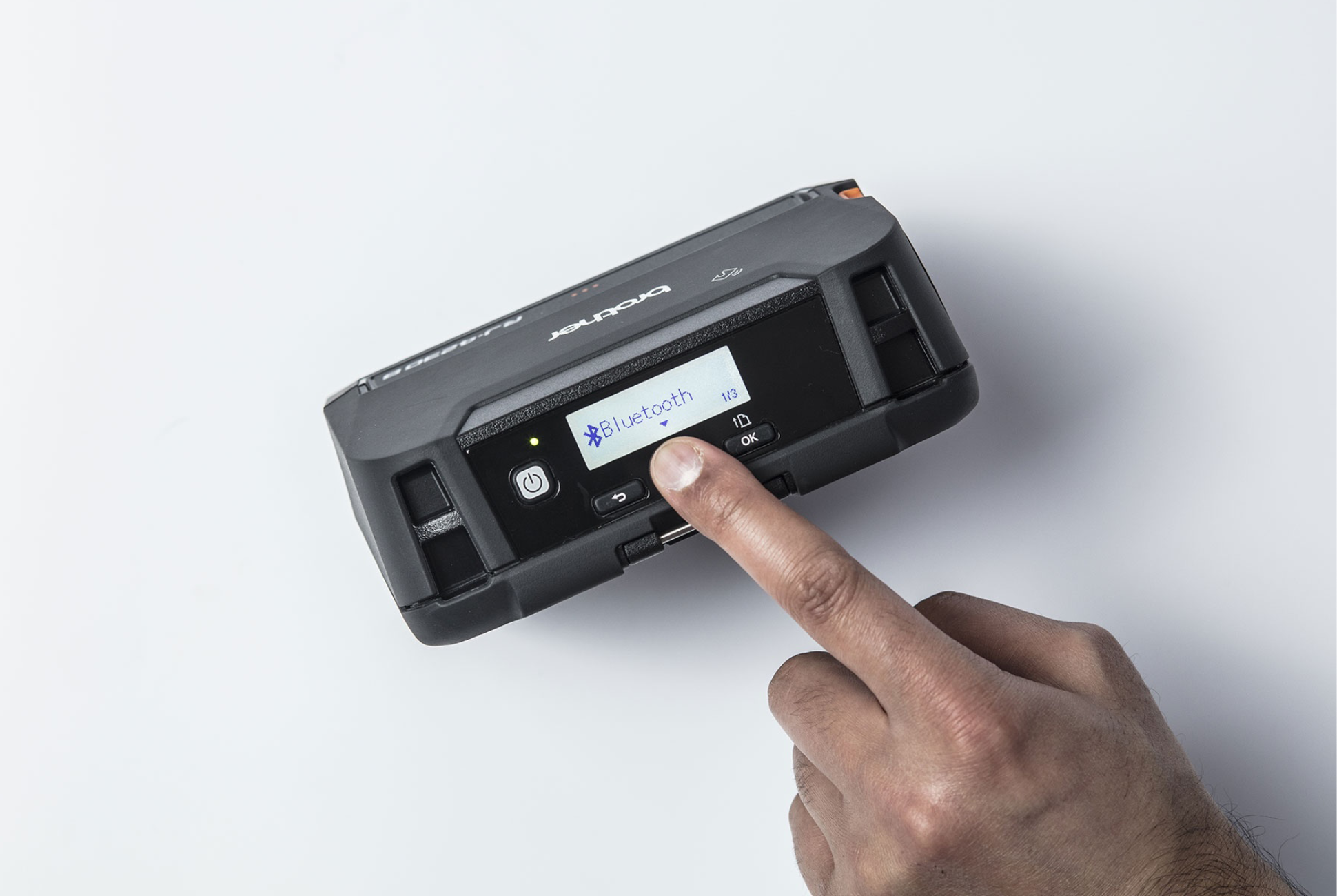 A hand presses a button on a black device displaying Bluetooth on its small screen.