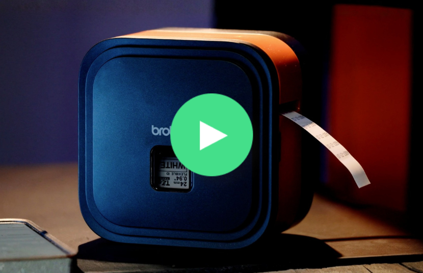 A portable label printer ejects a printed label; a green play button icon overlays the image.